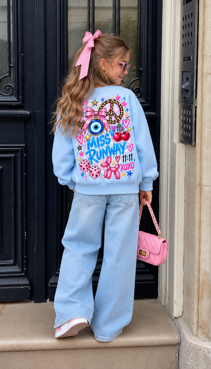 Back of the Cherry Charm kids' sweatshirt in baby blue with blue MISS RUNWAY lettering with a peace sign, an evil eye, cherries, a pink bow, disco balls and 11:11 XOXO – Miss Runway