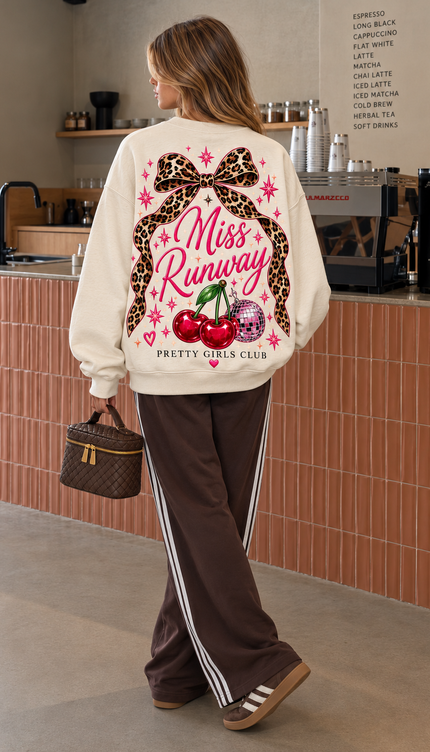 Back of the Cherry Cowgirl kids' sweatshirt in cream with Miss Runway script with a leopard print bow, cherries and a disco ball, finished with Pretty Girls Club – Miss Runway