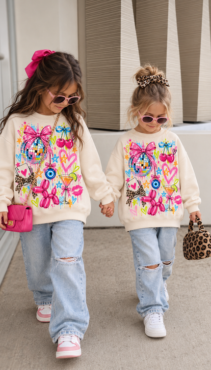 Front of the Disco Doll kids' sweatshirt in cream with a bright neon design of a disco ball tied with a pink bow, cherries, a leopard bow, a balloon dog, hearts, an evil eye, lips and a cocktail glass – Miss Runway