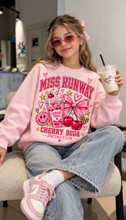 Girl wearing the Cherry Soda Sweatshirt in pink with a cherry soda and pink bow print by Miss Runway