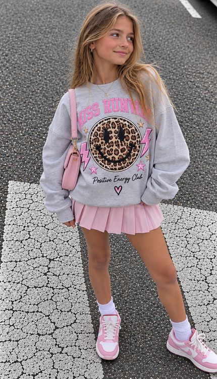 Girl wearing the Positive Energy Club Sweatshirt in grey with a leopard smiley print by Miss Runway