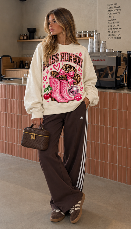 Front of the Cherry Cowgirl kids' sweatshirt in cream with pink MISS RUNWAY lettering with pink cowgirl boots, a leopard print cowboy hat, cherries and a disco ball – Miss Runway